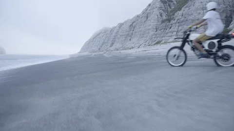 Slow motion shot of man driving motorbike on sandy beach near sea in morning Stock Footage 125836833
