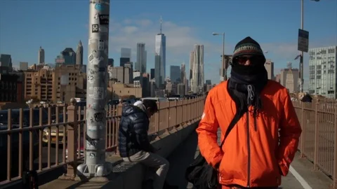 Slow motion shot of man in orange jacket with face concealed on Brooklyn Bridge Stock Footage 98666522