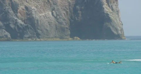Slow motion shot of man paddling on surfboard with rocks behind him, Japan Stock Footage 125828862