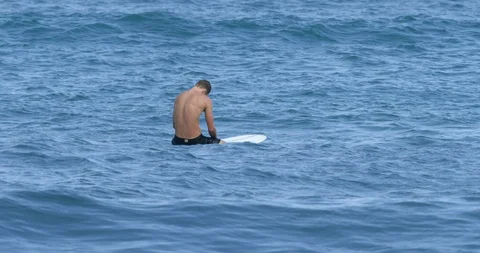 Slow motion shot of man sitting on surfboard watching sea around him, Japan Stock Footage 125836745