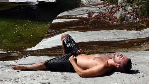 Slow motion shot of a man sleeping on the rocky banks of an alpine stream 動画素材 114178448