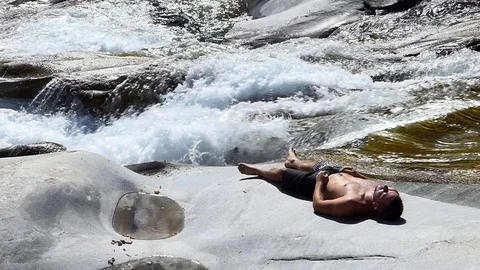 Slow motion shot of a man sleeping on the rocky banks of an alpine stream Stock Footage 114178494