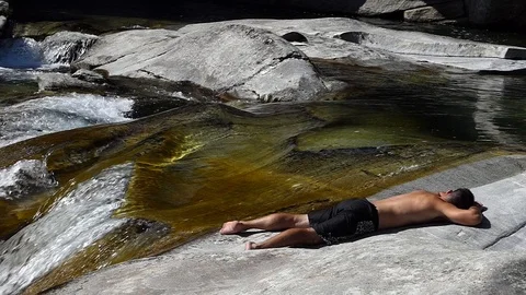 Slow motion shot of a man sleeping on the rocky banks of an alpine stream Stock-Footage 114178528