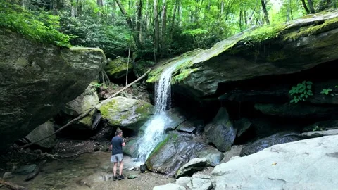 Slow motion shot of a man walking up to a waterfall Stock Footage 339810228