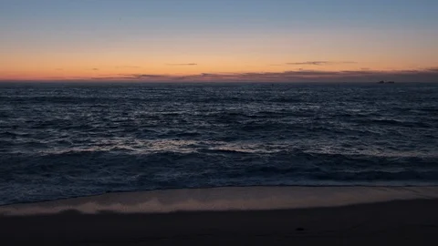 Slow motion shot over ocean at dusk with orange blue gradient sky, as bird flies Stock Footage 115758576