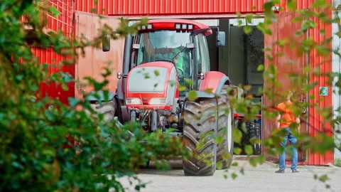Slow motion shot of a red tractor driving out of a barn on a rural farmyard Stock Footage 332960944