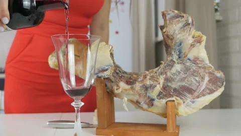 Slow motion shot of red wine pouring into a large glass. Jamon near a glass of Stock Footage 149140632