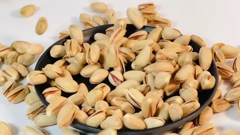 Slow motion shot of roasted pistachios falling onto a black plate Vídeos de archivo 336136986