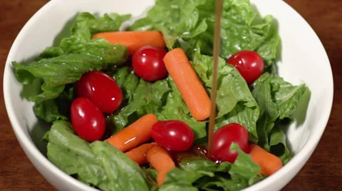 Slow motion shot of salad dressing being poured onto a salad on a wood table Видео 34664940