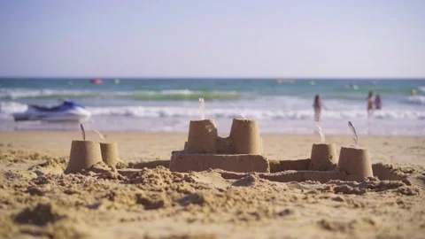 Slow motion shot of a sand castle on a beach, children running and playing Stock Footage 132923272