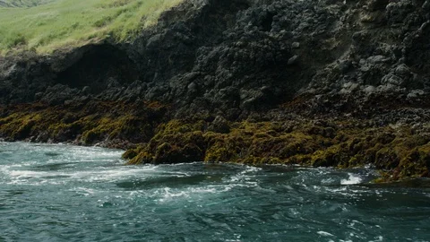 Slow motion shot of sea waves lapping on rocky shore with land in background Vidéo 123732041