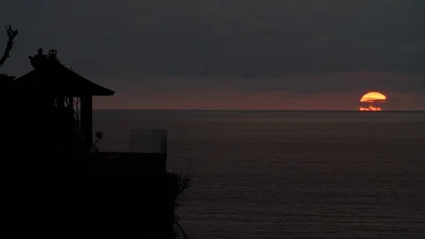 Slow motion shot of setting sun on dark sky with sea and hut in foreground, Bali Stock-Footage 140286155