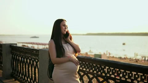 Slow motion shot. A soon-to-be mother chats on her phone while standing near the Video stock 249415491