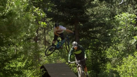 Slow motion shot of two guys mountain biking off a wood ramp. Video stock 77577870