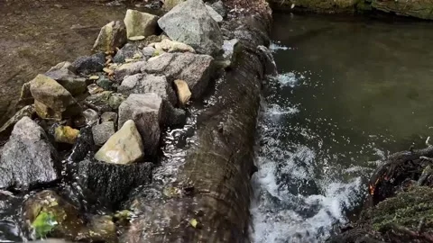 Slow-motion shot of water flowing over an artificial weir made of logs and st Видео 343911535
