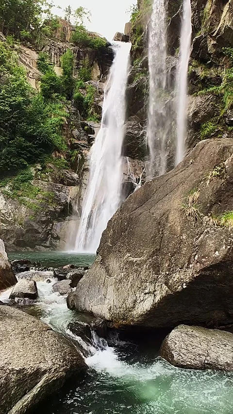 Slow-motion shot of a waterfall between brown rocks and lush green forest Stock Footage 248074450