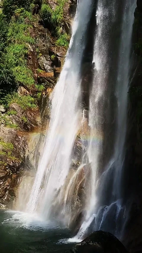 Slow-motion shot of a waterfall between brown rocks and lush green forest Stock Footage 248378225