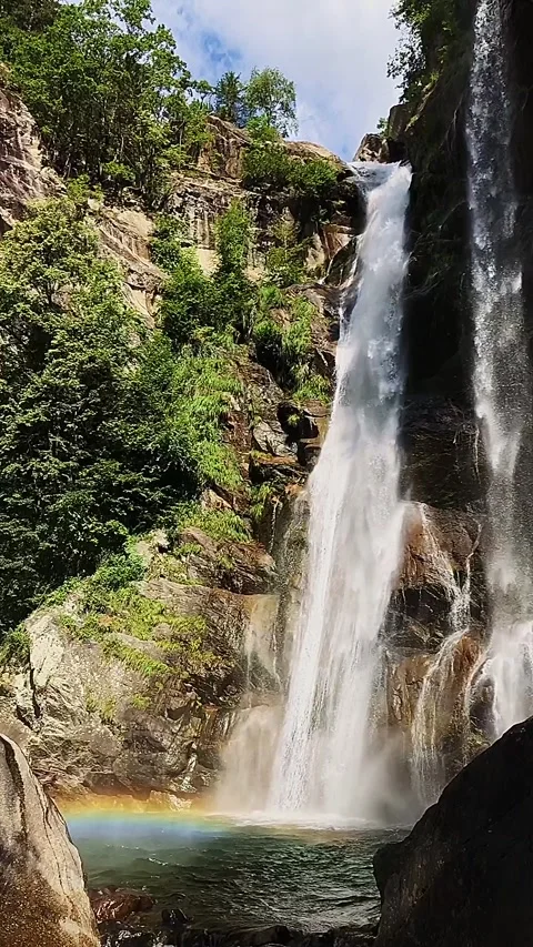 Slow-motion shot of a waterfall between brown rocks and lush green forest Stock Footage 248378274