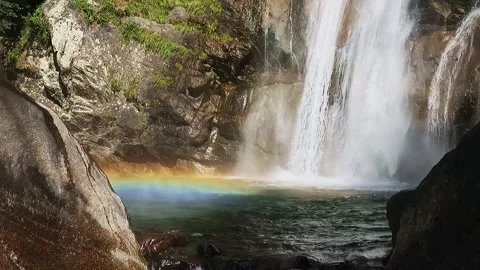 Slow-motion shot of a waterfall between brown granite rocks and green forest Video stock 248379030