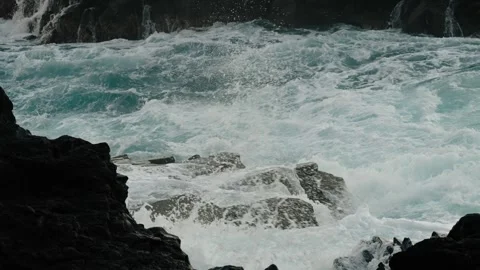 Slow-motion shot of waves exploding against jagged volcanic rocks and concrete Stock Footage 312030576