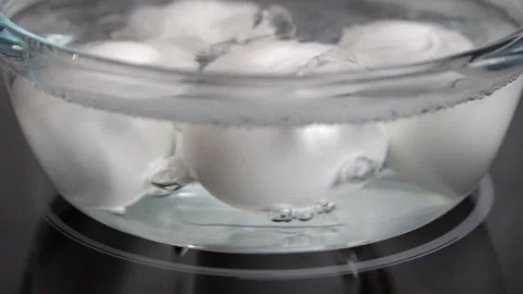 Slow motion shot of white eggs boiling in a transparent glass pot on an ele.. Stock Footage 254730102