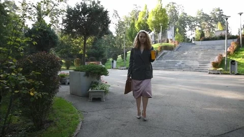 Slow motion shot of a young blonde woman walking through a park 库存影片 333058503