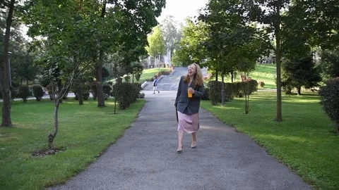 Slow motion shot of a young blonde woman walking through a park 库存影片 333058616