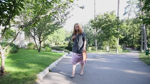 Slow motion shot of a young blonde woman walking through a park 库存影片 333070490