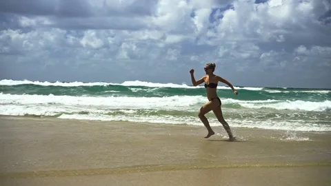Slow-motion shot of a young energetic woman in swimsuit running along ocean Stock Footage 307523978