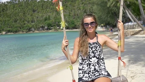 Slow motion shot of a young happy smiling woman having fun on a swing on beach Stock Footage 74642611