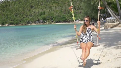 Slow motion shot of a young happy smiling woman having fun on a swing on beach Stock Footage 74642617