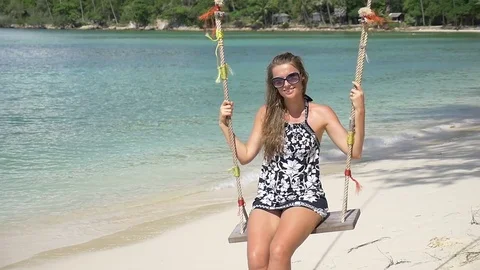 Slow motion shot of a young happy smiling woman having fun on a swing on beach Stock Footage 74642631