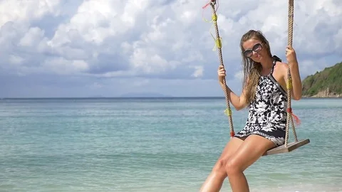 Slow motion shot of a young happy smiling woman having fun on a swing on beach Stock Footage 74642666