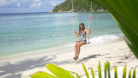 Slow motion shot of a young happy smiling woman having fun on a swing on beach Stock Footage 74642671