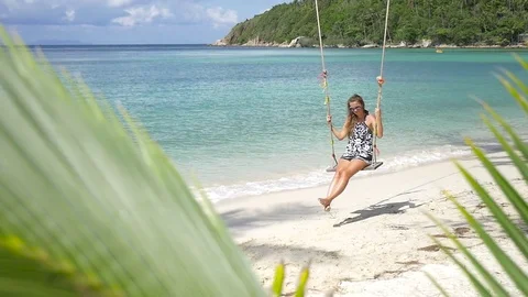 Slow motion shot of a young happy smiling woman having fun on a swing on beach Stock Footage 74642677