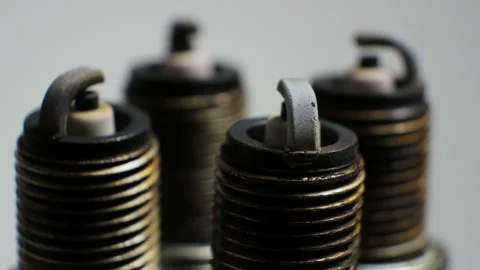 Slow motion showcases a set of used and dirty spark plugs arranged on a white Video stock 290464782