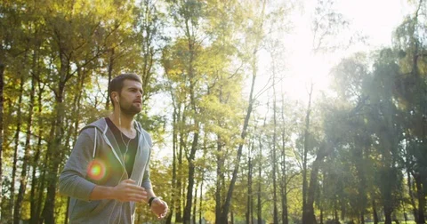 Slow motion from the side and below of young sporty man in headphones jogging in Stock Footage 82503695