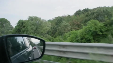 Slow motion side mirror view captures passing countryside and guardrail from Stock Footage 341694035