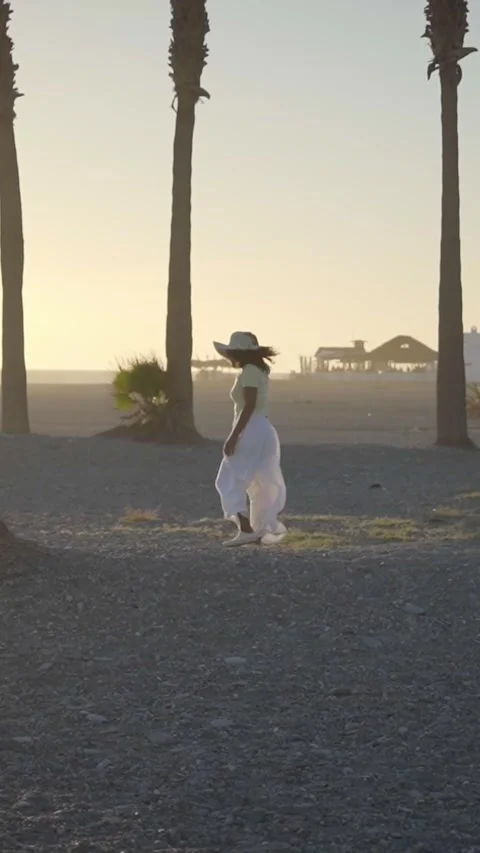 Slow motion side view of African young woman in hat walking on beach at golden Stock Footage 274136394