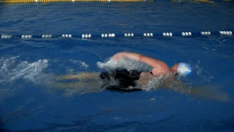 Slow motion side view of female swimmer in cap and goggles swimming in a pool Stock Footage 119762896