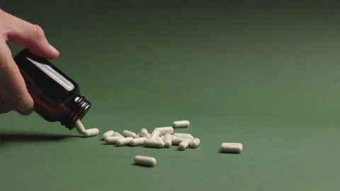 Slow motion side view of man pouring medicine pills on green background Stock Footage 343449840