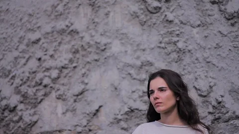 Slow Motion Side View Sad Lonely Brunette Stands Against a Gray Stone Wall and Stock Footage 73597637