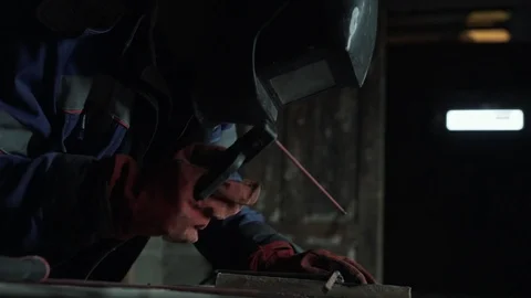 Slow-motion, side view welder in welding mask welds two metal parts. Workman in Stock Footage 105823882