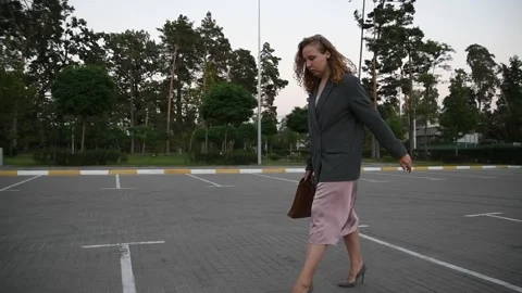 Slow motion side view of a young blonde woman walking across an empty parking Vidéo 333070861