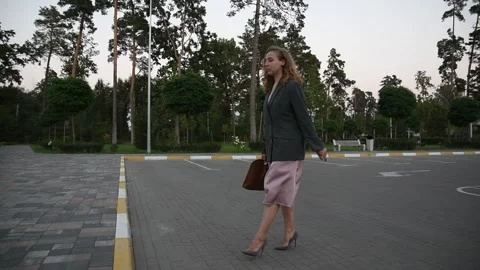 Slow motion side view of a young blonde woman walking across an empty parking Vídeos de archivo 333070874