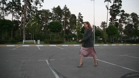 Slow motion side view of a young blonde woman walking across an empty parking Vídeos de archivo 333070879