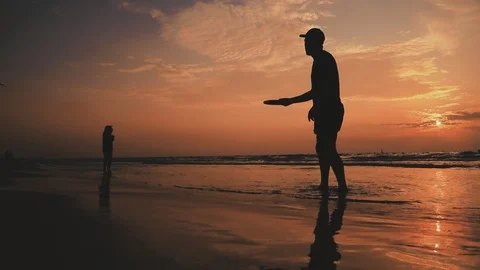 SLOW MOTION. Silhouette people playing with frisbee on the beach backlit by Stock Footage 118568153