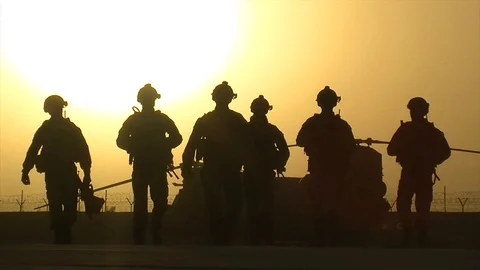 Slow motion of silhouette of soldiers walking at a base in Afghanistan at sunset Stock Footage