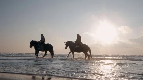 SLOW MOTION. silhouette of women riding beautiful horses wading through the sea Stock Footage