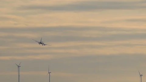 Slow-motion: silver-gray jet plane taking a turn, flying over wind turbines Stock Footage 96353840